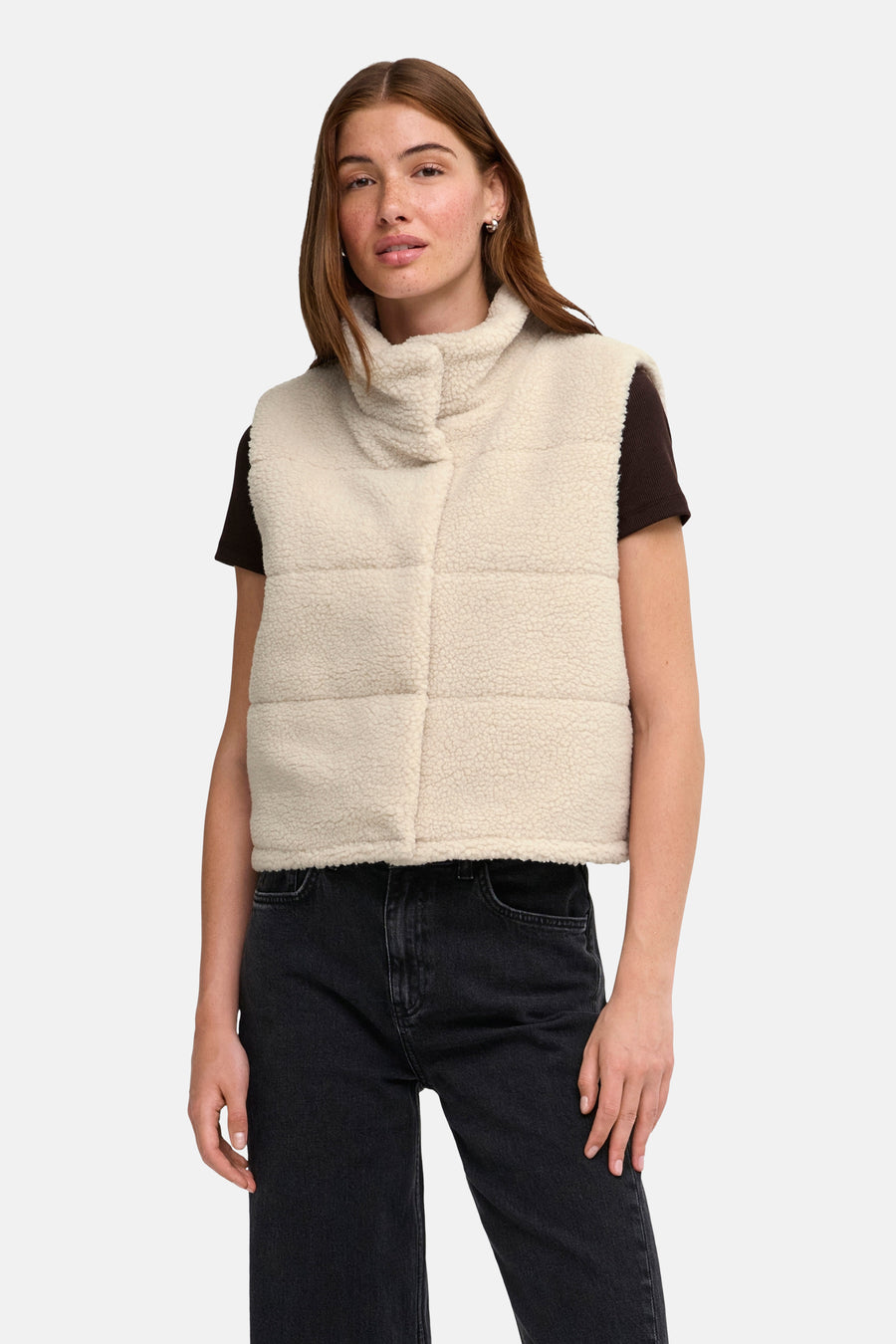 Doudoune sans manches couleur crème en tissu en peau de mouton avec fermeture éclair, de la marque ONLY®, portée sur un t-shirt foncé et un jean noir, vue de face
