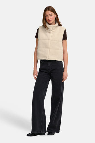 Doudoune sans manches couleur crème avec texture brossée et col montant de la marque ONLY®, portée sur un t-shirt foncé, avec un jean large noir et des mocassins, vue de face.