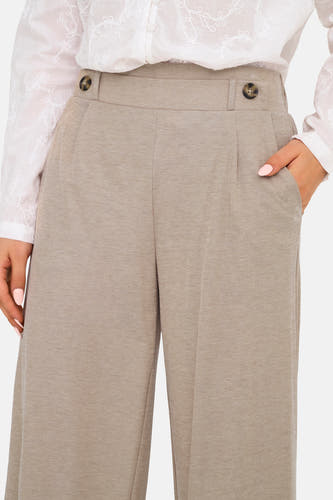 Pantalon beige de JDY avec boutons, plis et poches italiennes, porté avec une blouse blanche brodée.
