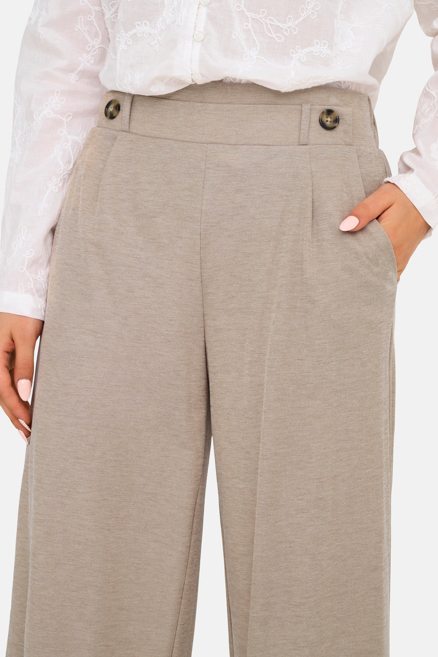 Pantalon beige de JDY avec boutons, plis et poches italiennes, porté avec une blouse blanche brodée.