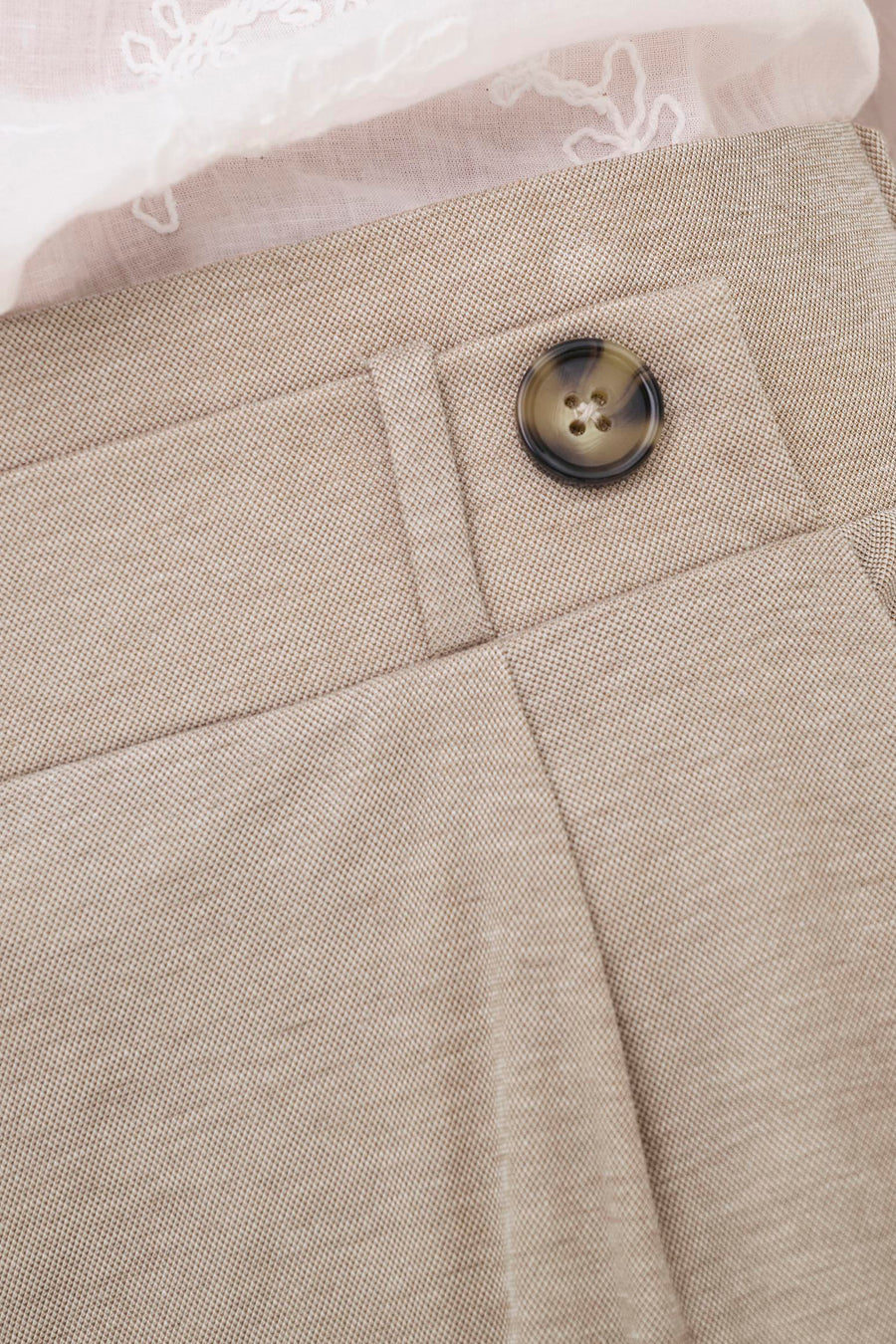 Pantalon beige de JDY avec un bouton marron, une texture fine et un haut en dentelle blanche par-dessus.