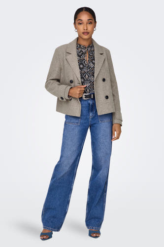 Manteau court beige ONLY, avec une double rangée de boutons, porté avec une blouse et des jeans bleus.