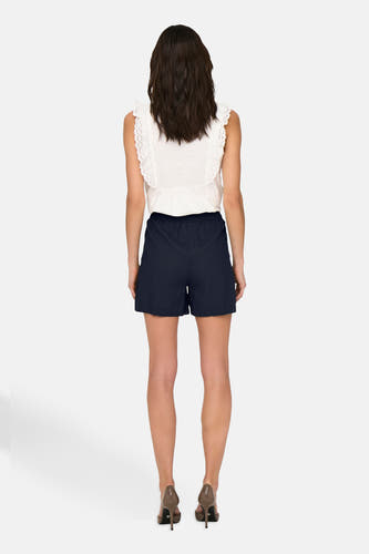 Donkerblauwe short van JDY, gezien van achteren, gecombineerd met een witte top met kanten details en hoge hakken.
