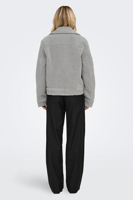 Manteau court gris d'ONLY, avec texture en fourrure de teddy, porté avec un pantalon noir, dos.