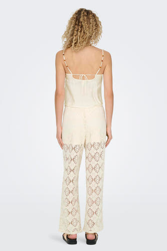 Ecru mouwloze blouse van ONLY, met dunne bandjes en opengebreide broek.
