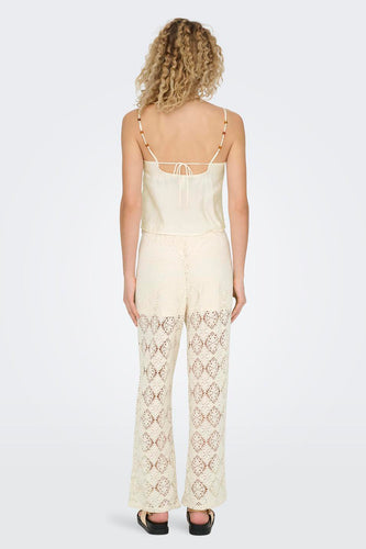 Achterkant van een vrouw in een crèmekleurige top en gehaakte broek.