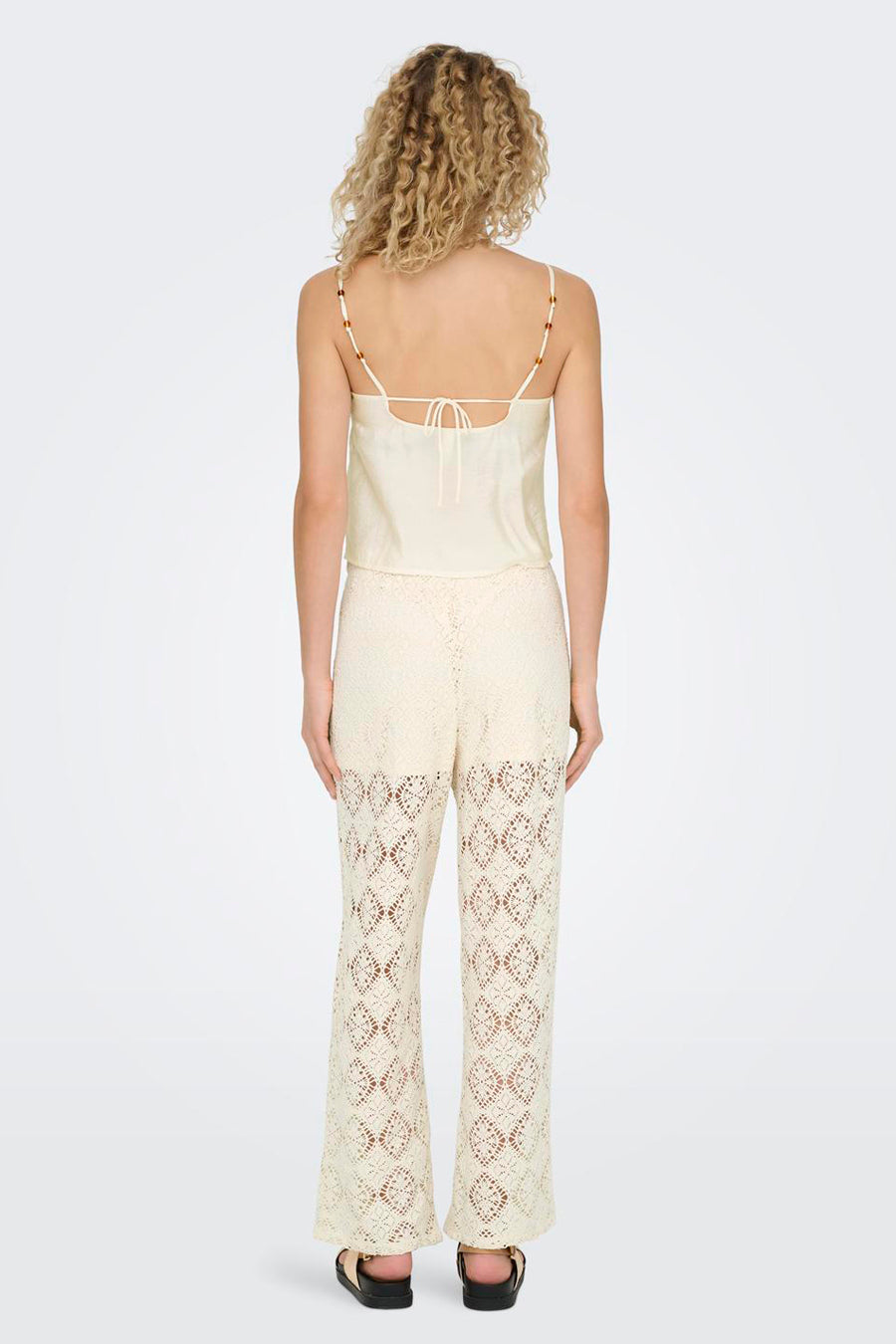 Achterkant van een vrouw in een crèmekleurige top en gehaakte broek.