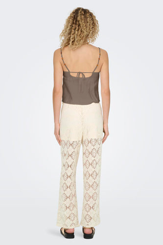 Achterkant van een vrouw in een bruine top en witte gehaakte broek, staand op een witte achtergrond.