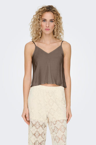 Vrouw met gekruld blond haar, bruine top en gehaakte witte broek.