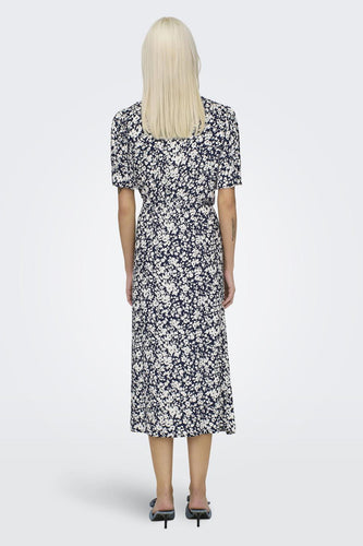 Achterkant van een vrouw in een blauwe bloemenjurk.