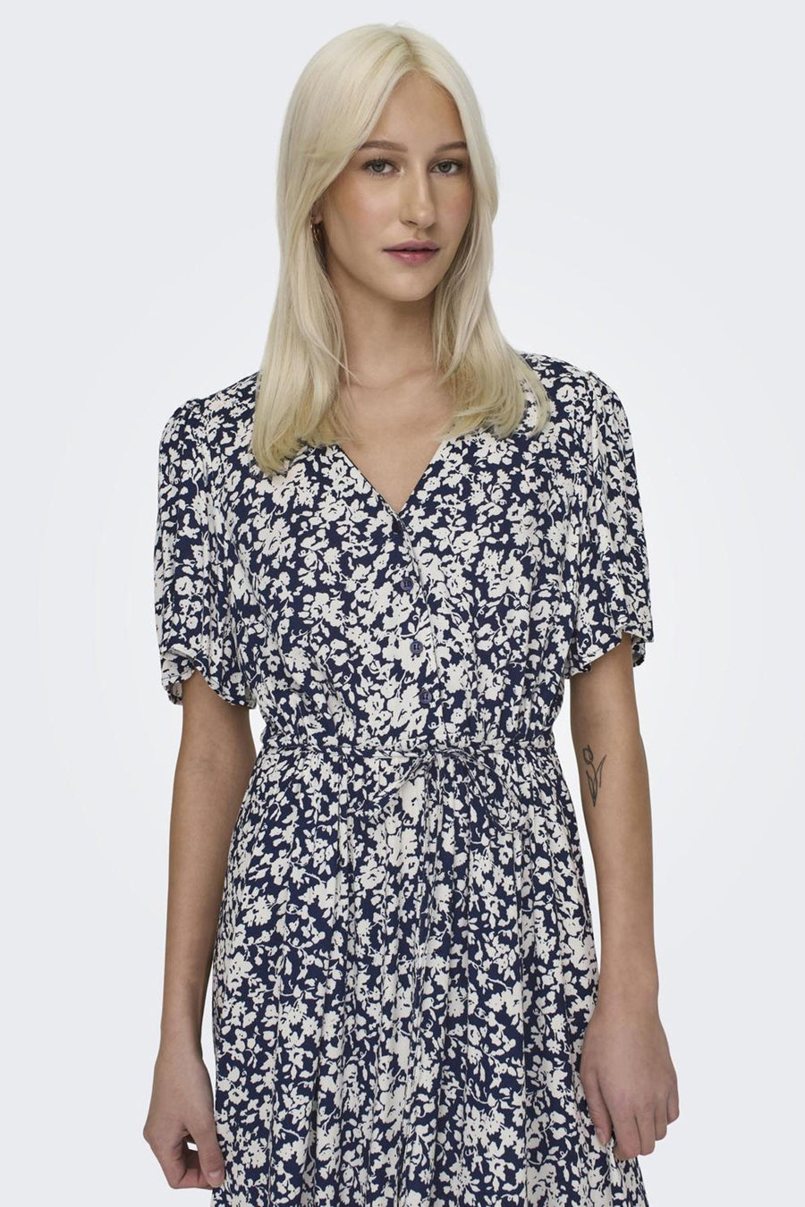 Vrouw in marineblauwe bloemenjurk met knopen en strikceintuur.