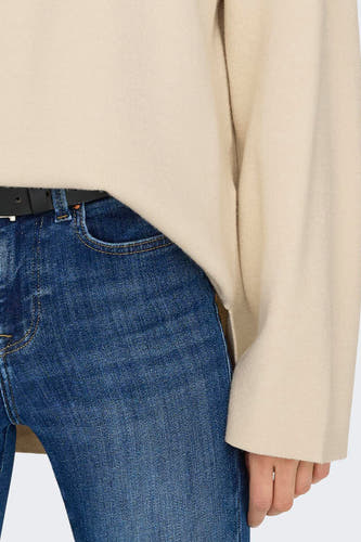 Pull écru avec col rond de ONLY, avec des manches longues et porté avec des jeans bleus et une ceinture noire.