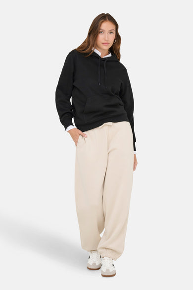 Pull-over noir avec capuche ONLY, associé à un pantalon de jogging beige et des baskets blanches.