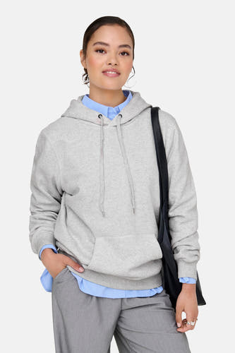 Pull-over gris avec capuche ONLY, porté sur une chemise bleue et un pantalon gris avec un sac noir.
