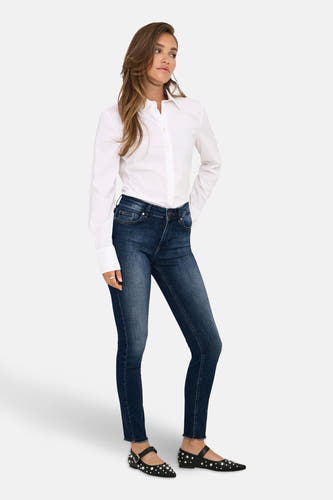 Jean skinny en denim bleu marine de ONLY, avec des coutures visibles et porté avec un chemisier blanc et des ballerines noires.