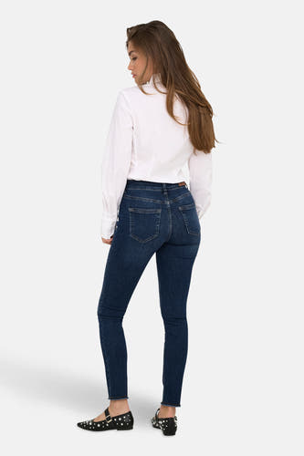 Jean skinny en denim bleu marine de ONLY, porté avec un chemisier blanc et des ballerines noires pailletées.