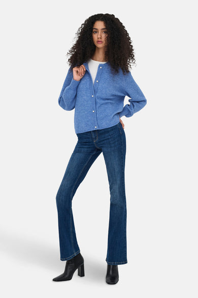 Veste bleue de JDY, avec des boutons en nacre, portée sur une chemise blanche et un jeans foncé avec des bottes.