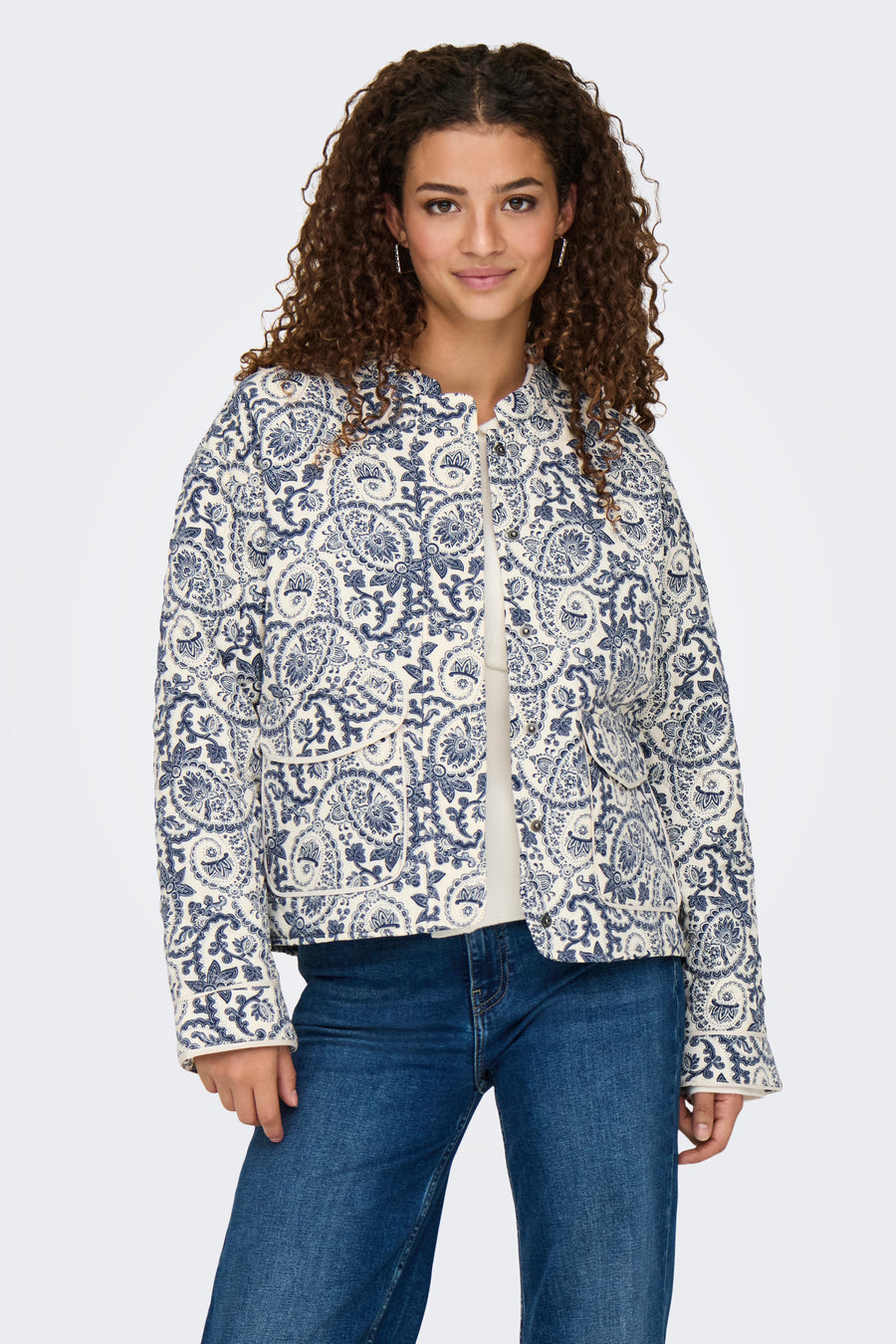 Manteau bleu de ONLY à motif cachemire, porté sur un gilet crème à boutons et un jean bleu.