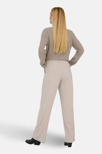 Vrouw met blond haar draagt beige trui en pantalon.