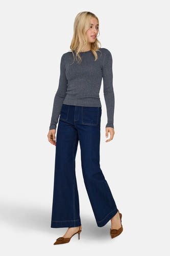 Femme en un pull gris, un pantalon bleu marine large et des escarpins marrons.