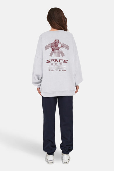 Pull-over gris ONLY avec l'impression "Space Adventure" sur le dos, associé à un pantalon de jogging bleu foncé et des baskets blanches.