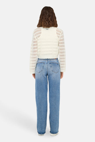 Achterkant van een vrouw in een witte gehaakte top en blauwe jeans op een witte achtergrond.