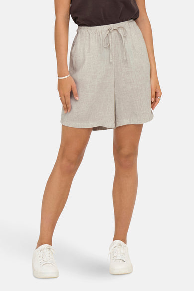 Ecru short van ONLY, met trekkoord in de taille en gecombineerd met witte sneakers en zilveren armband.
