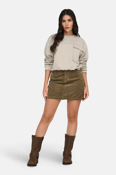 Bruine korte rok van JDY, met corduroy textuur, gecombineerd met een beige sweater en bruine laarzen.
