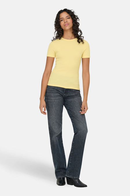 Een vrouw in een geel shirt en donkere jeans.