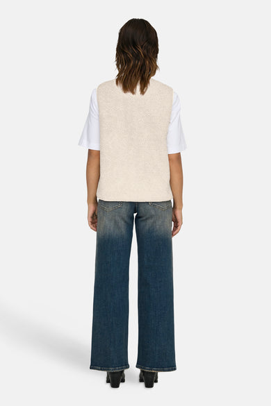 Gilet écru de ONLY, avec une texture en fourrure de teddy, associé à un t-shirt blanc et des jeans larges, vu de dos.