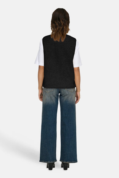 Gilet noir ONLY, porté sur un t-shirt blanc avec des jeans bleus larges et des bottines noires.