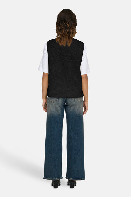 Gilet noir ONLY, porté sur un t-shirt blanc avec des jeans bleus larges et des bottines noires.