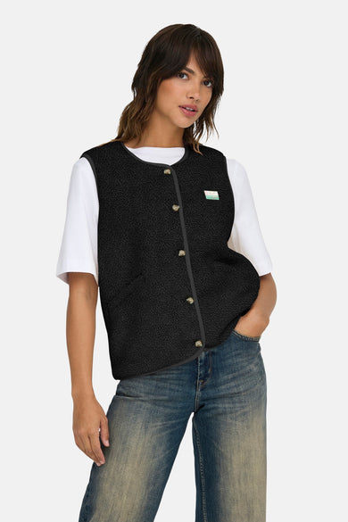 Gilet bodywarmer noir d'ONLY, avec fermeture à boutons et une étiquette sur la poitrine, porté sur un T-shirt blanc et des jeans.