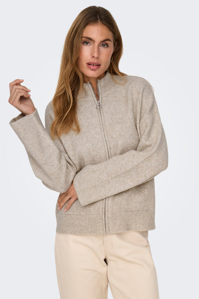Gilet écru de JDY, avec une fermeture à glissière à l'avant et porté sur un pantalon beige.