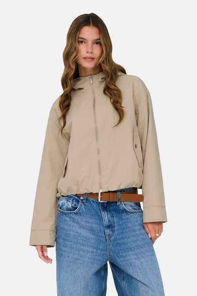 Beige jas van ONLY, gedragen met blauwe jeans en een bruine riem.
