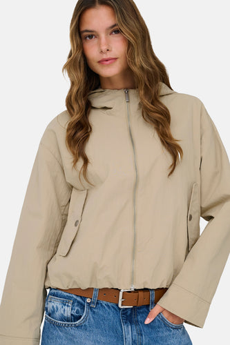 Beige jas van ONLY® met lange mouwen, ritssluiting en een bruine riem over een jeans.
