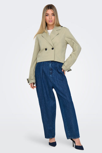 Vrouw in beige jas en wijde jeans, poseert in studio.