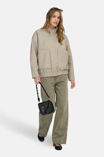 Beige korte jas van ONLY, met opgestikte zakken, gedragen met groene broek en zwarte handtas.