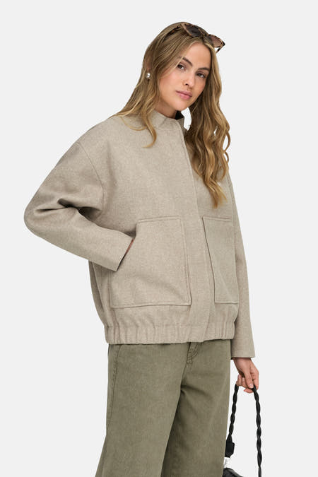 Manteau beige de ONLY®, avec poches et porté avec un pantalon vert.