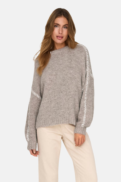 Gilet rond beige de JDY, avec des points blancs sur les manches, porté avec un pantalon crème.