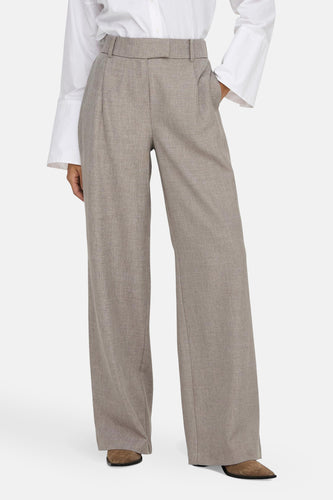 Kostuumbroek in beige, van ONLY®, met wijde pijpen en een subtiele textuur, gecombineerd met een wit overhemd.
