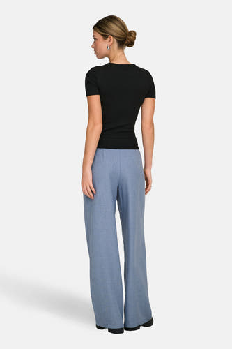Pantalon de costume bleu ONLY, avec des jambes larges et porté avec un chemisier noir.
