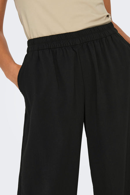 Pantalon noir de ONLY, avec une ceinture élastique et une main dans la poche.
