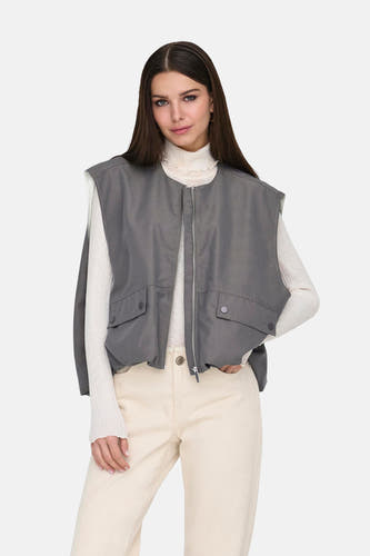 Gilet gris ONLY, avec des poches, porté sur une veste blanche et un pantalon beige.