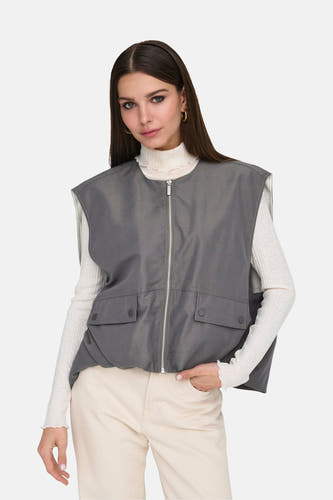 Gilet gris ONLY® avec fermeture éclair et poches, porté sur une veste blanche et un pantalon beige.