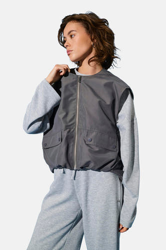 Gilet gris ONLY, avec fermeture éclair argentée et poches brodées, porté sur un pull gris et un pantalon de jogging.