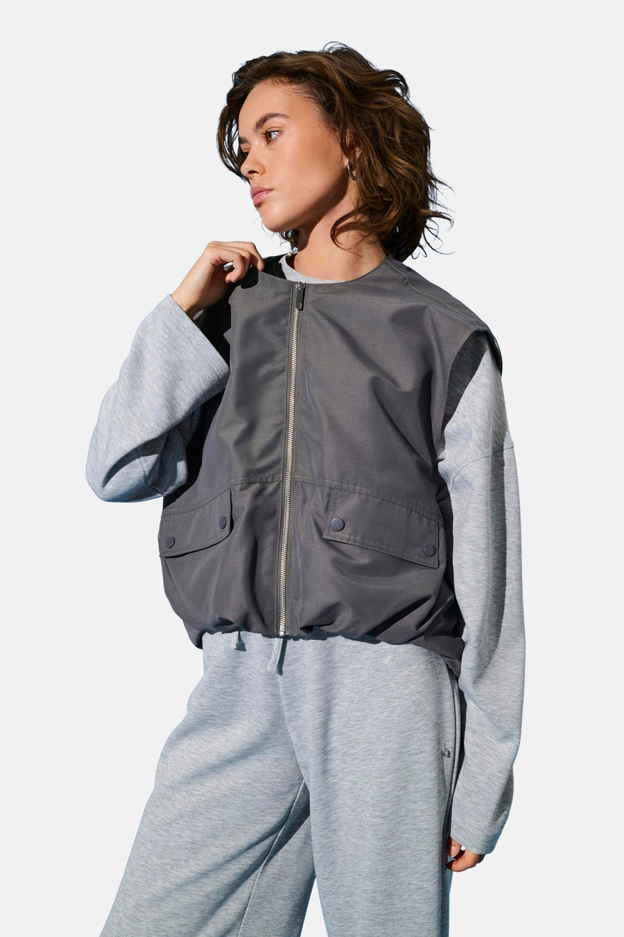 Gilet gris ONLY, avec fermeture éclair argentée et poches brodées, porté sur un pull gris et un pantalon de jogging.