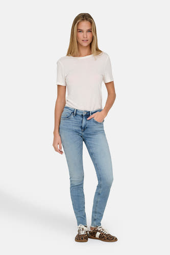 Jean skinny bleu clair d'ONLY, avec une légère usure et associé à un T-shirt blanc et des baskets à imprimé animal.
