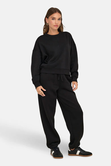 Pull-over noir de ONLY, porté avec un pantalon de jogging coordonné et des baskets noires.