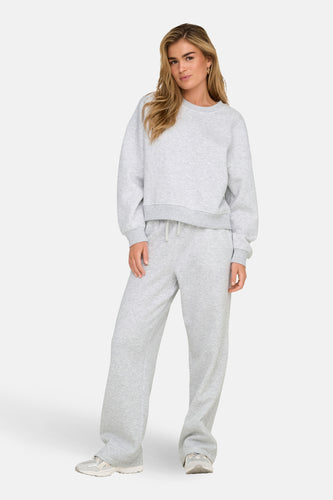 Vrouw in grijze joggingbroek en sweater.